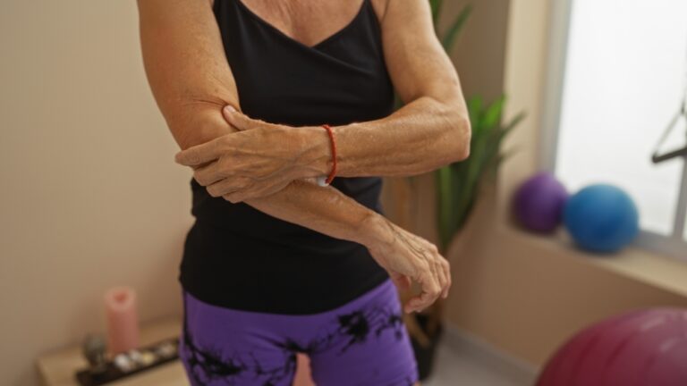 middle-aged woman in yoga pants and tank top in the middle of a workout holding her elbow because it hurts