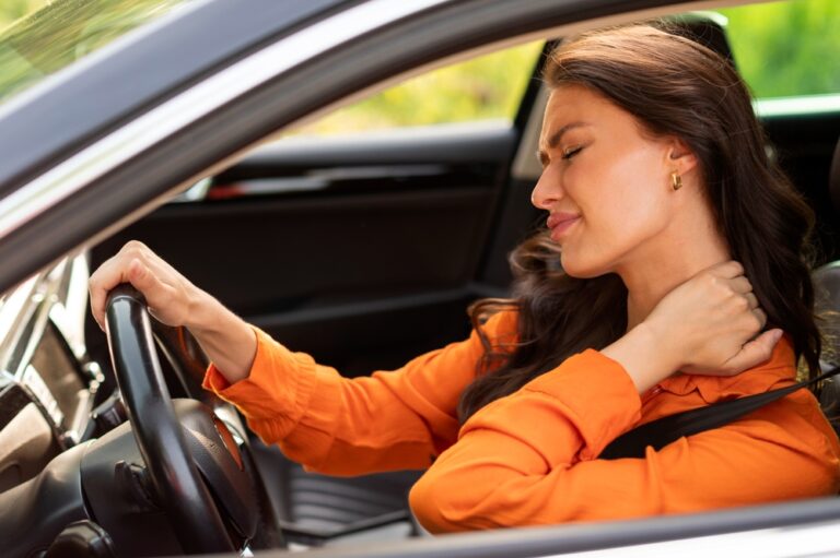 woman sitting in the driver's seat of her car and massaging her neck