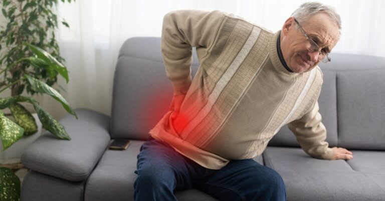 man suffering from lower back pain as he sits on the couch