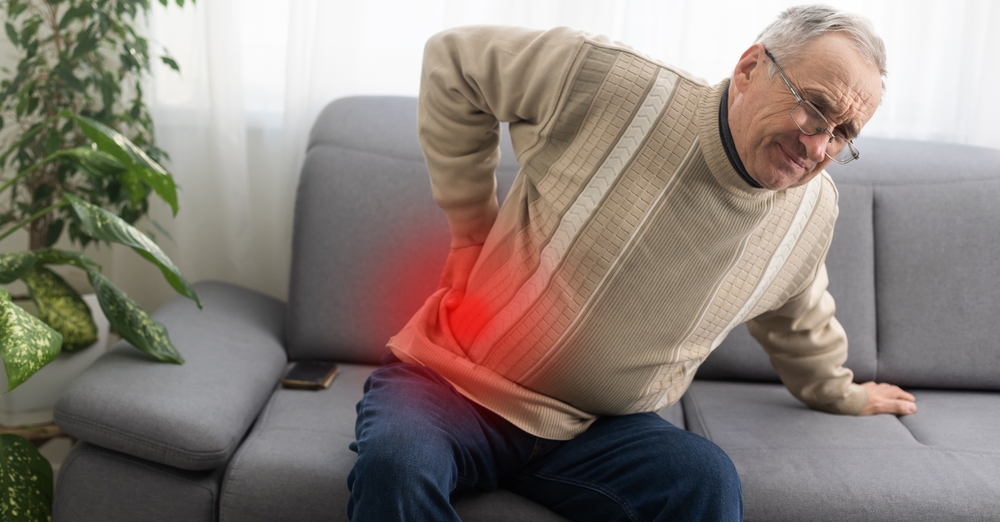man suffering from lower back pain as he sits on the couch